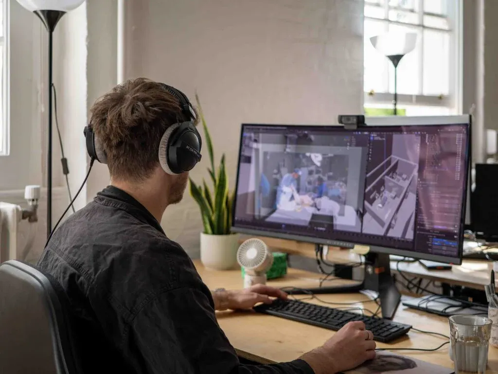A man wearing headphones working at a desk, viewing a 3D architectural model on a computer screen.